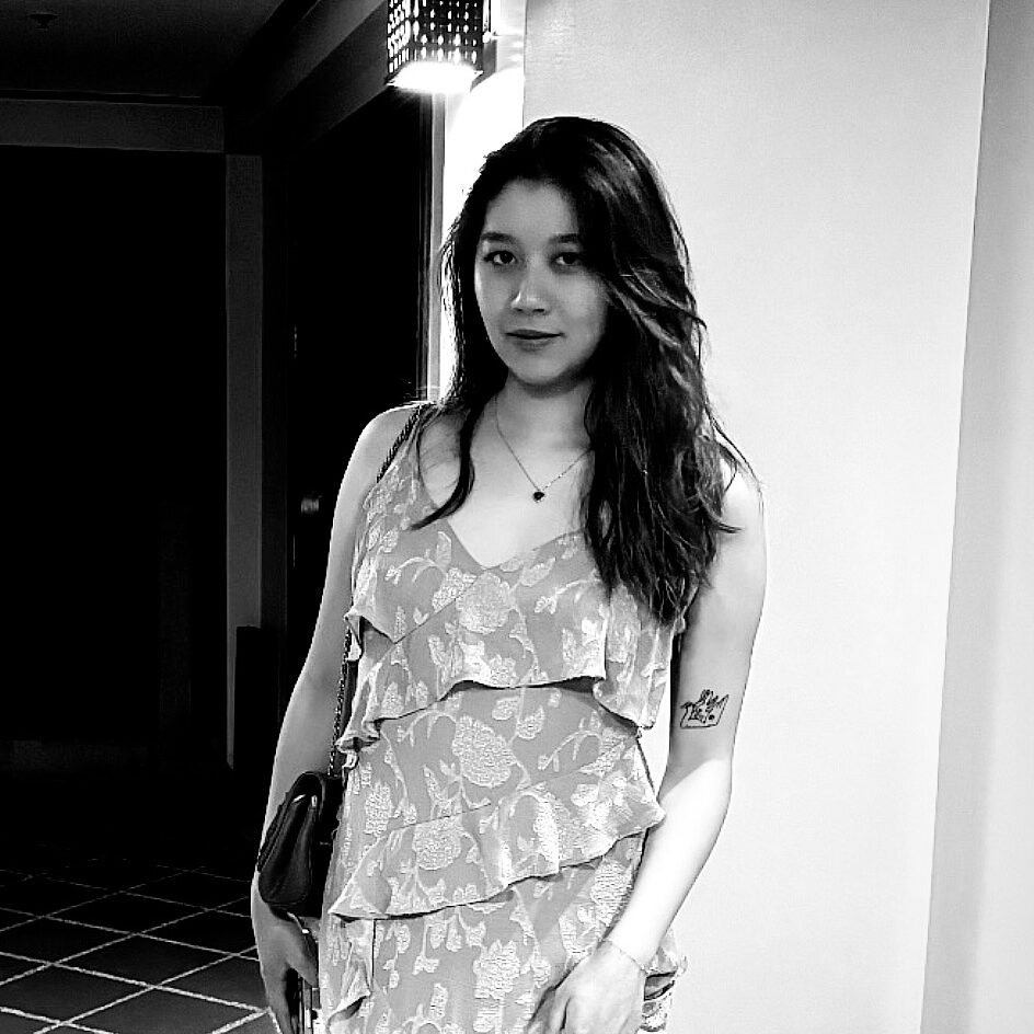 Screenshot Black-and-white photo of an Asian woman with long hair wearing a patterned ruffle dress and holding a small purse.