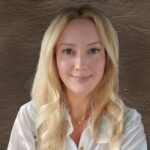 Ana Mourant headshot. Ana has long blond hair, blue eyes, and is wearing a white shirt. She is smiling warmly.