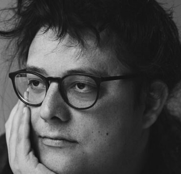 Black and white photo of author with dark glasses and hair