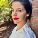 Laura Page leaning against a brick wall with the woods in background.