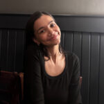 Megan sits in front of a paneled wall, tilting her head to the side and smiling at the camera.