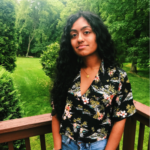 a headshot of Neha Peri. She is standing against a brown deck with trees and grass in the background