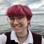 Headshot of Dorie Palmer. They are smiling in front of a lake.