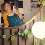 Mirror selfie of a tattooed, bespectacled blonde woman in a teal dress with white polka dots.