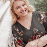 an author photo for Samantha Edmonds, which shows her leaning against a brick wall and smiling in a green dress.