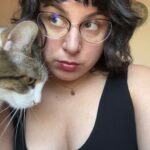 An image of Jess trying out a new lip gloss/liner combo while looking demurely to the side, while her cat, Turkey, is half in frame.