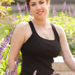 photo of a woman in a black dress sitting on a bench among flowers.