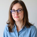 A woman with shoulder-length brown hair and tortoiseshell-patterned glasses against a neutral background