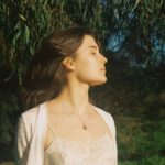 Girl stands in the sun under a eucalyptus tree with her eyes closed.