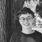 black and white photo of Sara, a white genderqueer person, with a tree in the background