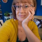 Blonde woman with oversized glasses, a yellow sweater, and a mischievous glint in her eye